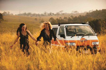 A couple running through a field next to a Hippie Camper. 